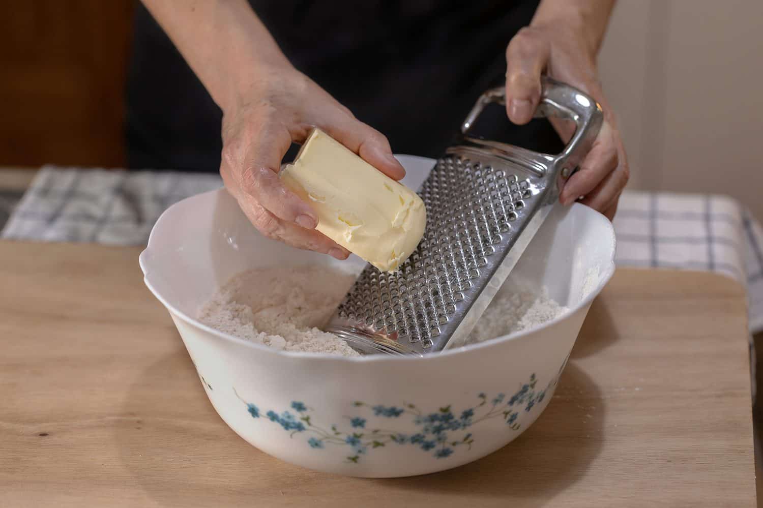 Female hands grating a pat of butter over some flour in a bowl.