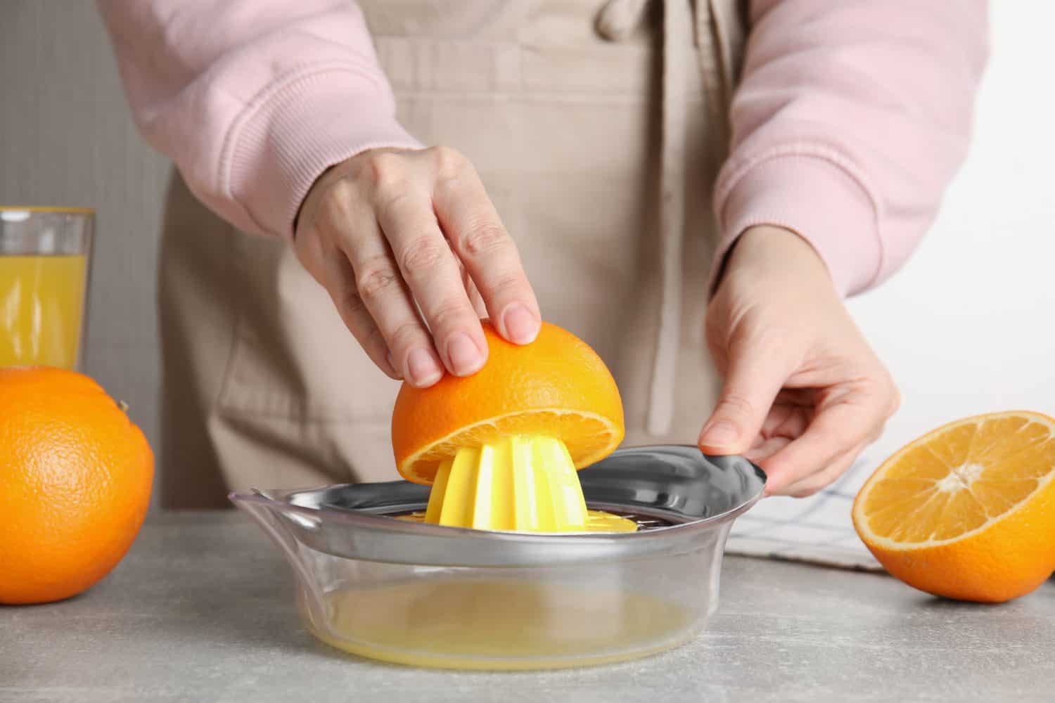 Woman squeezing orange juice at grey table, closeup