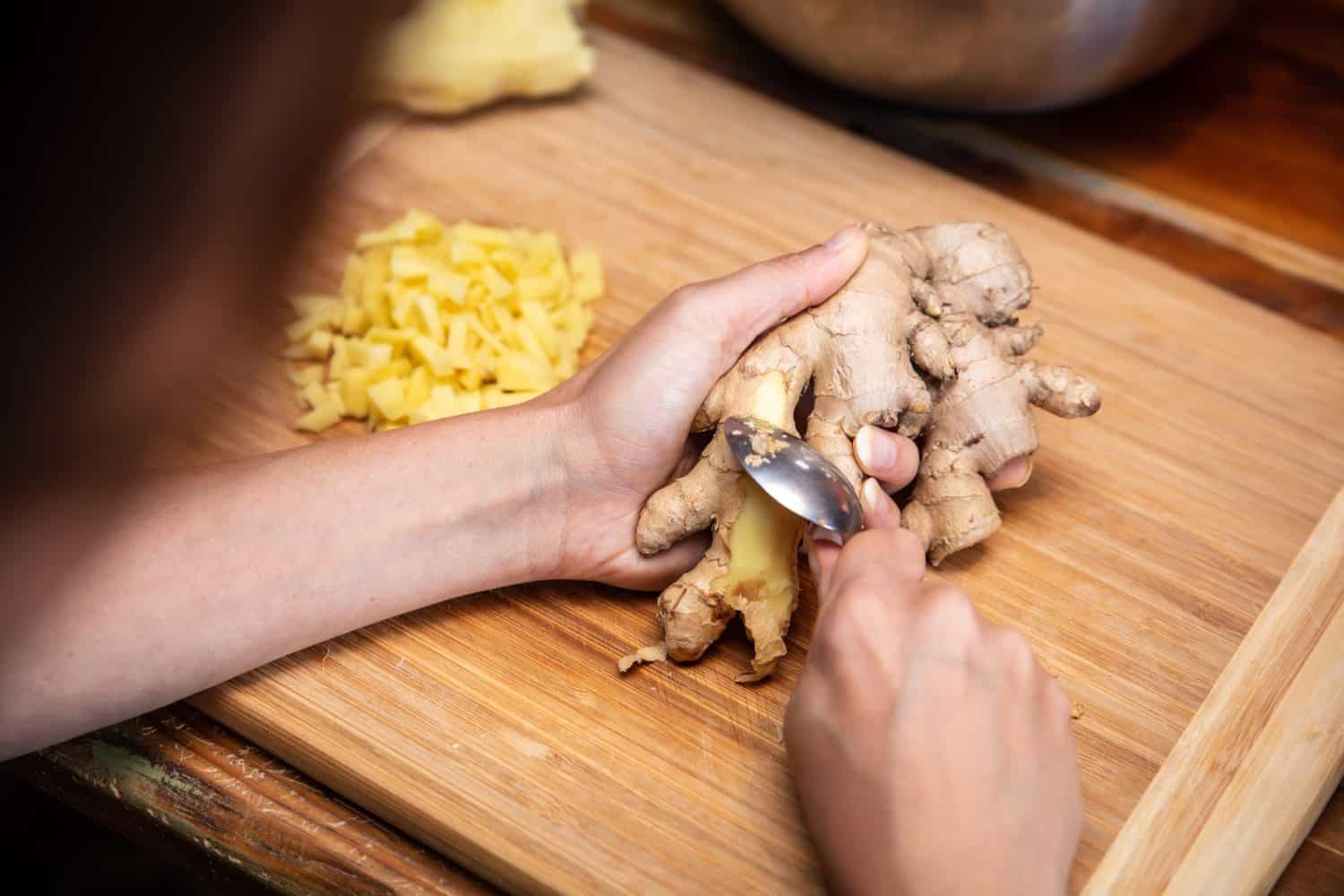 Peeling or peel off ginger with a spoon, preparation in the kitchen, female hands
