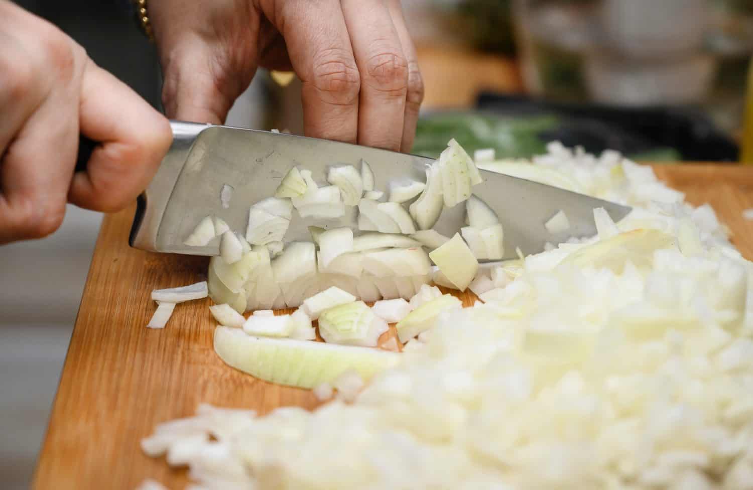 A woman holds a large sharp knife in her hand and cuts the onion into small pieces.