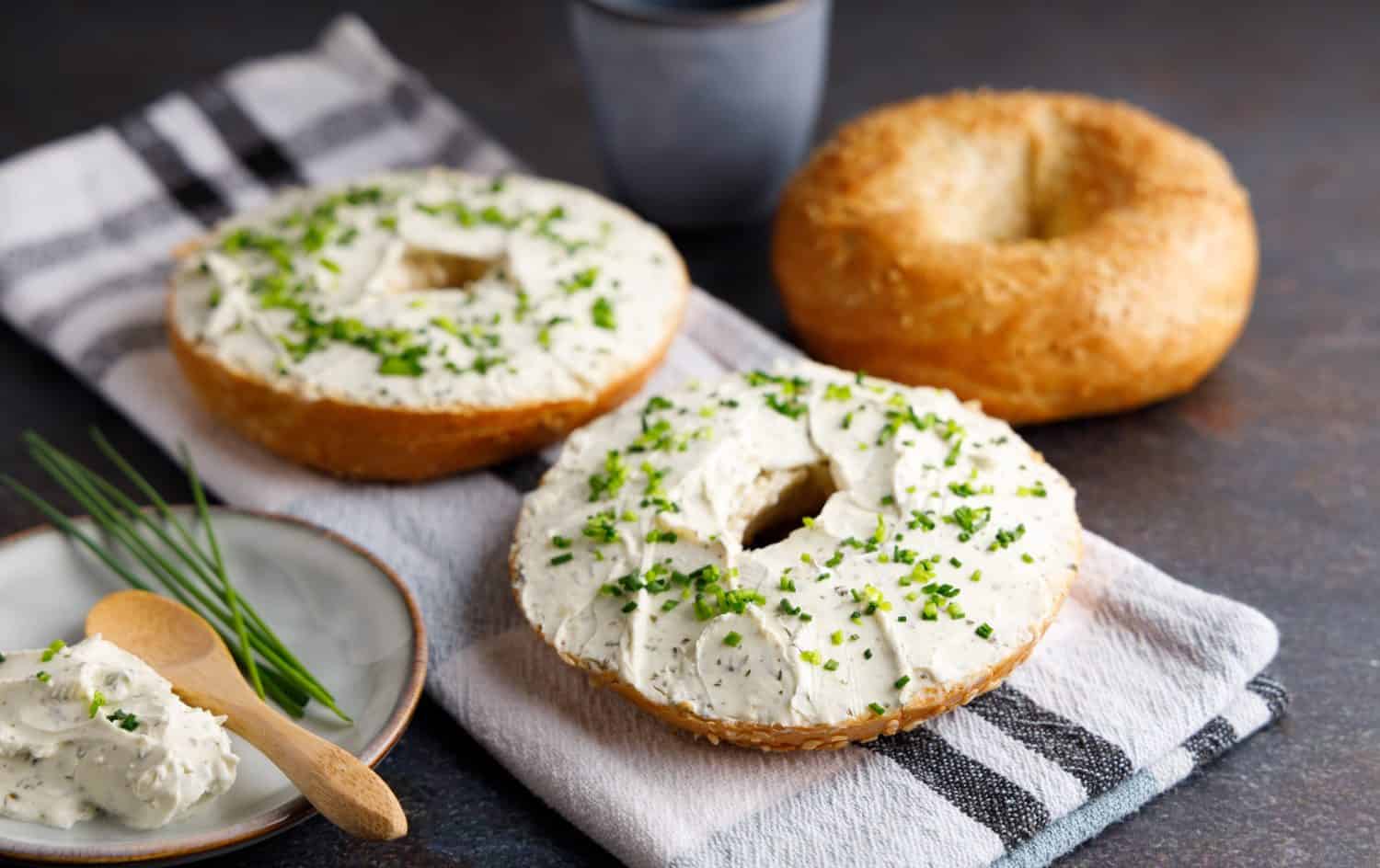 Bagels with fresh cheese and herbs on a breakfast table , with fresh orange juice and coffee on the side.