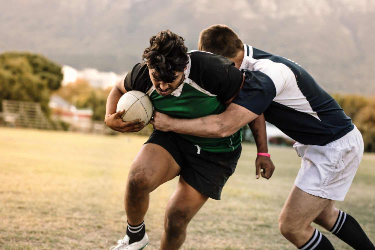 Professional rugby players striving to get the ball during the game. Rugby player with ball is blocked by the opposite team player at ground.