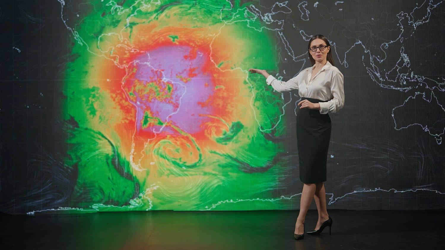 Female presenter in the studio. Woman anchor news host presenting weather forecast, reporting on air, virtual climate map graphic background at the back.