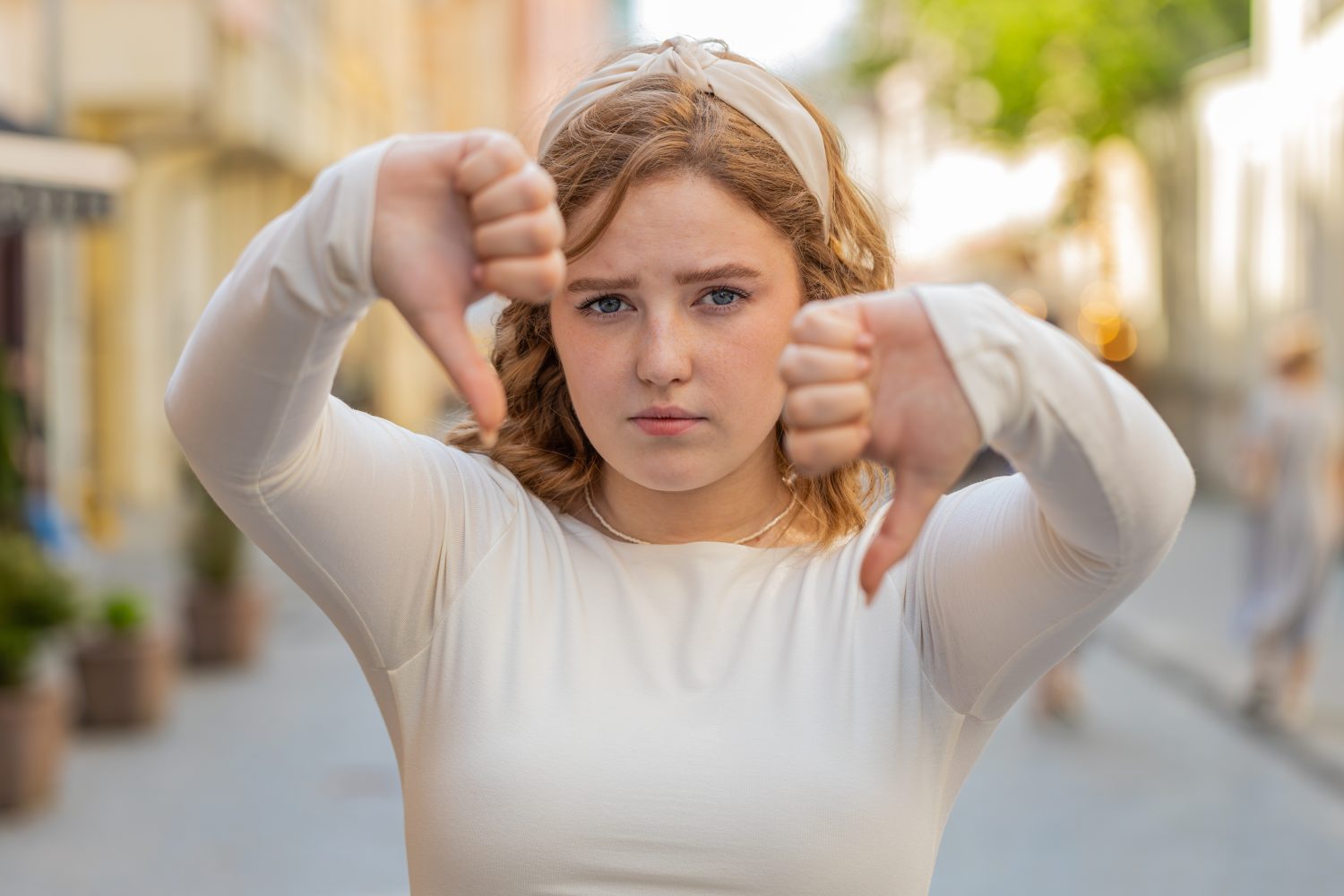Dislike. Upset redhead young woman showing thumbs down sign gesture, expressing discontent, disapproval, dissatisfied bad work, mistake outdoors. Displeased girl in urban city street. Town lifestyles.