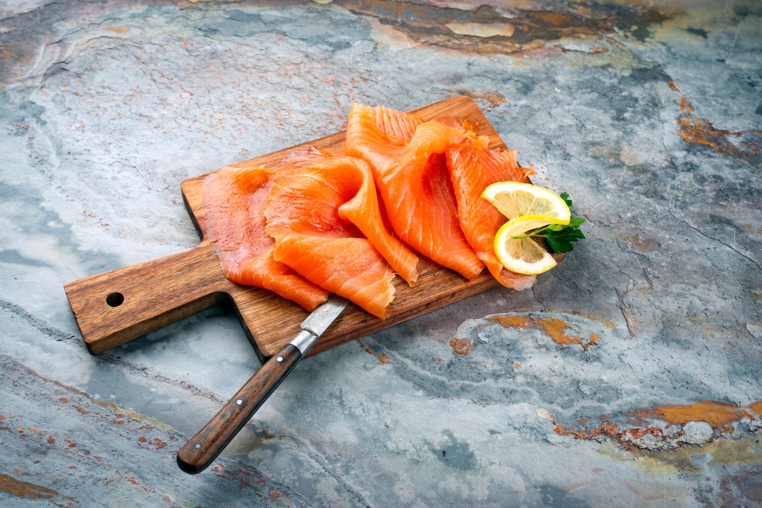Traditional Norwegian smoked salmon in slices with parsley and lemon served as a close-up on a rustic wooden chopping board with text space