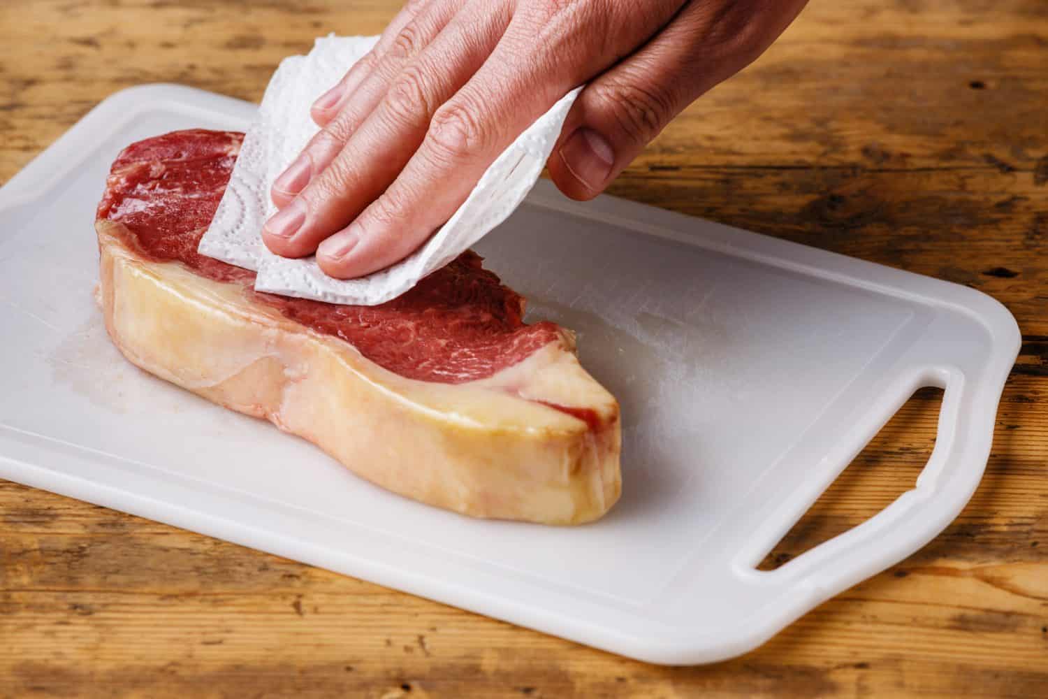 Raw fresh meat Steak Striploin on cutting board drying up excess moisture by Male hand with paper towel