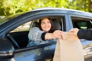 Cheerful obese woman smiling while buying fast food at a drive thru while driving her car