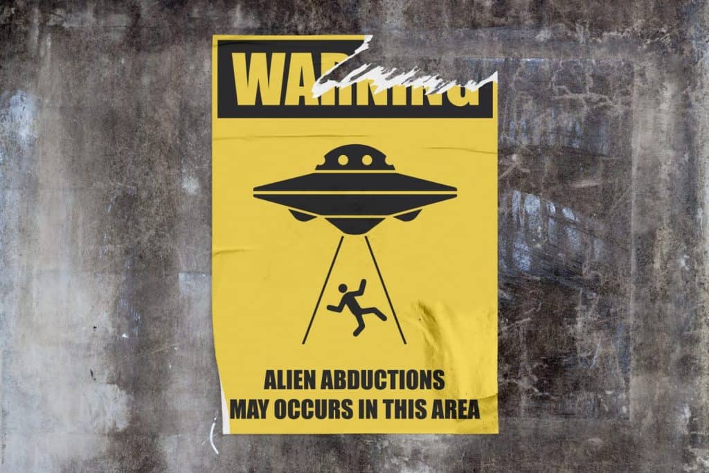 Full-frame weathered concrete wall with a torn yellow poster in the middle depicting an UFO abducting a man with 