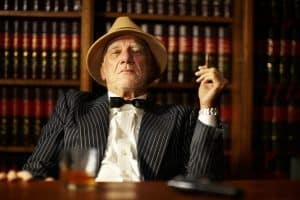 Portrait, mafia and boss with cigarette in office for habit, smoking or relaxing by desk. Mature, mob leader and retro fashion in suit, bowtie and hat for crime, danger or power with vintage look