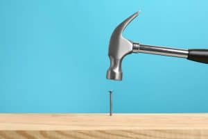 Hammering nail into wooden surface against light blue background