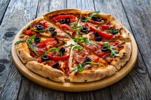 Circle pizza nduja with mozzarella, black olives and arugula leaves on wooden table