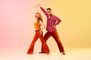 Artistic, expressive man and woman in stylish clothes dancing disco, retro dance against gradient pink yellow background. Concept of retro style, dance, fashion, art, hobby, music, 70s, hobby