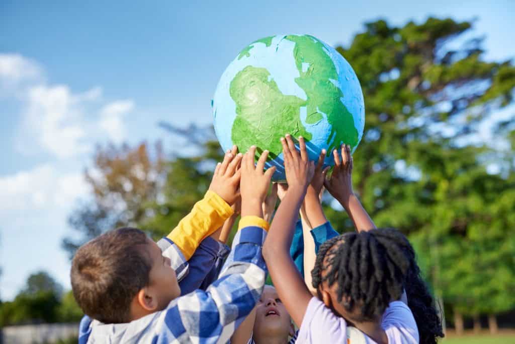 Group of multiethnic children holding model of earth in park with copy space. Primary students holding a big handmade earth model and raising it high. Save the planet, earth day and global peace.