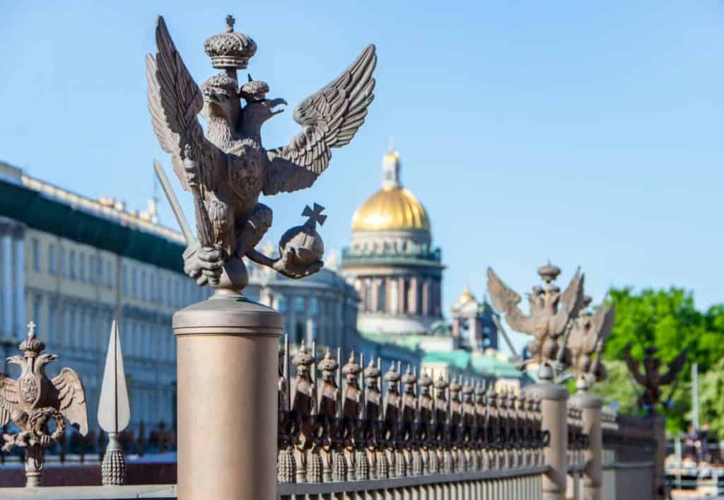 Double-headed eagle on the fence of the Alexander Column at the Winter Palace and a view of St. Isaac's Cathedral (blurred focus), St. Petersburg, Russia