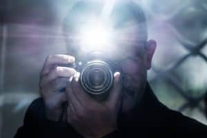 a man looks into the camera's viewfinder and takes pictures using a flash, a photographer on the background of a metal grating, a selfie in a gloomy room
