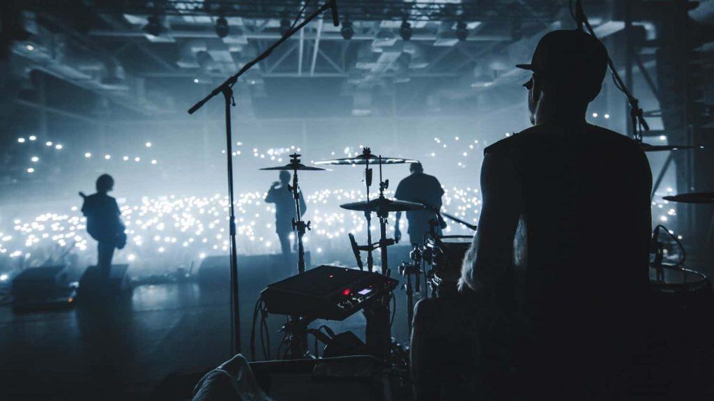 Music band group silhouette perform on a concert stage. silhouette of drummer playing on drums audience holding cigarette lighters and mobile phones