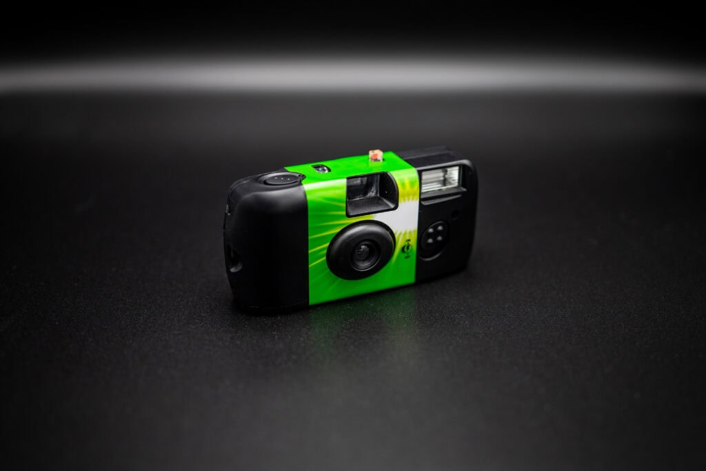 Green disposable film camera on a black background