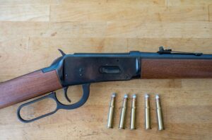 Detail of an old winchester lever-action rifle from the wild and far west with some 30-30 caliber bullets on a wooden table