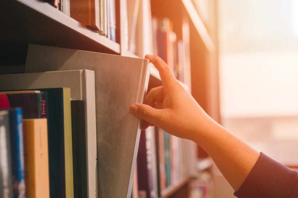 Hand picking a book or takes out from the shelf, pulling book from bookshelf in public library in university, college or high school in Education and literature concept