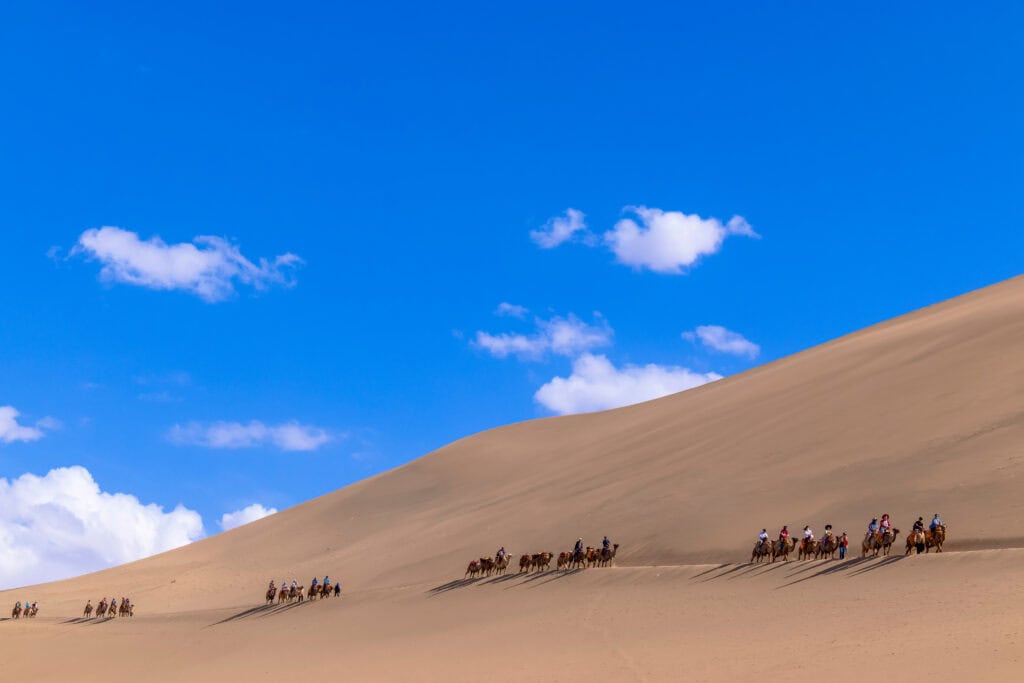 Group of tourists are riding camel at the sand mountain Mingsha Shan desert or the singing sand dunes with the caravan as part of the Silk Road in Dunhuang, Gansu, China.