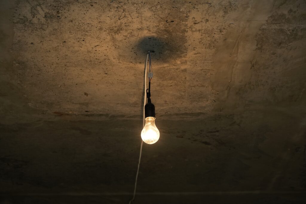Dim light bulb on grey concrete ceiling of basement or bomb shelter. Electric lamp. Temporary lighting from a mobile generator.