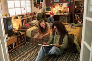 Two young adults sitting on the floor of a well-decorated bedroom, engaging in an intellectual discussion and sharing ideas, while surrounded by various retro items such as books, gadgets, and posters