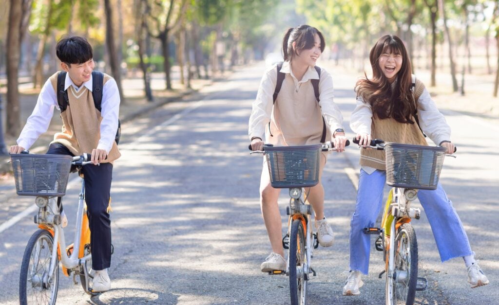 Happy teenager students riding bicycle at the school