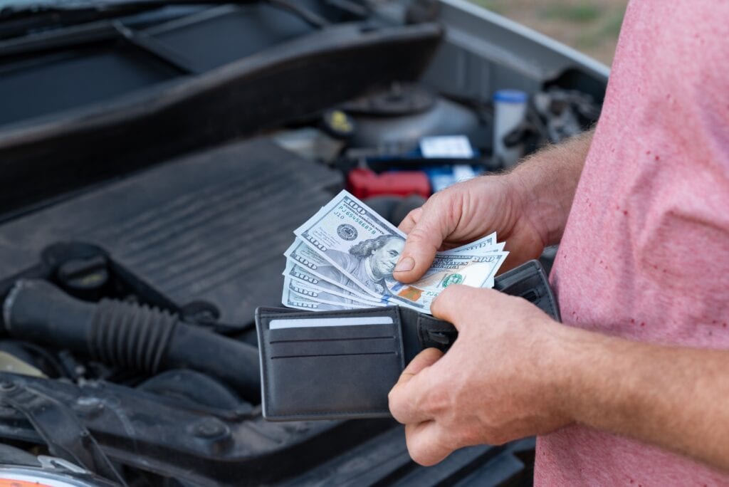 Customer taking dollar banknotes of his wallet to pay for car repair. Spending money for repair at car service, high price for spare parts and fixing