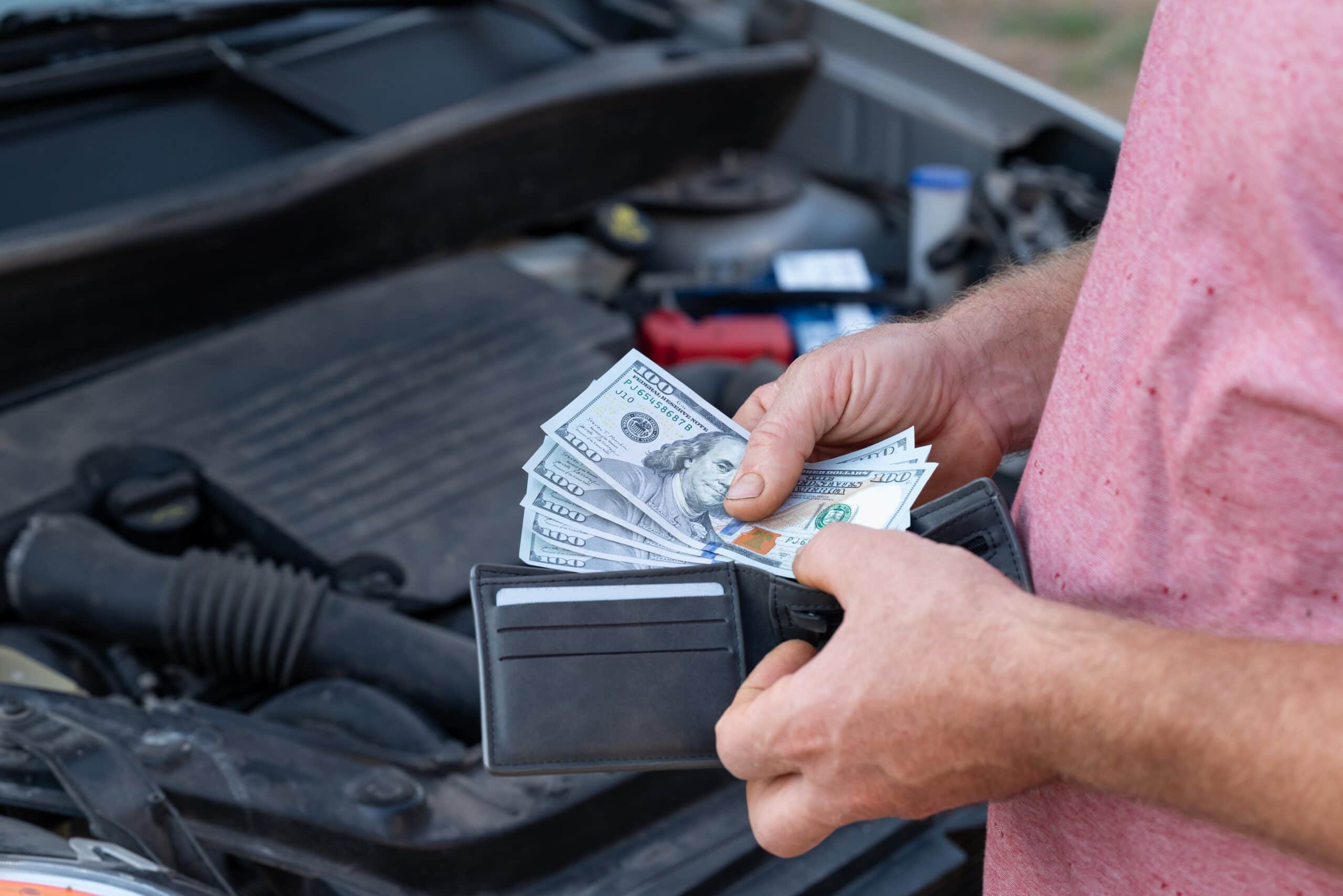 Customer taking dollar banknotes of his wallet to pay for car repair. Spending money for repair at car service, high price for spare parts and fixing
