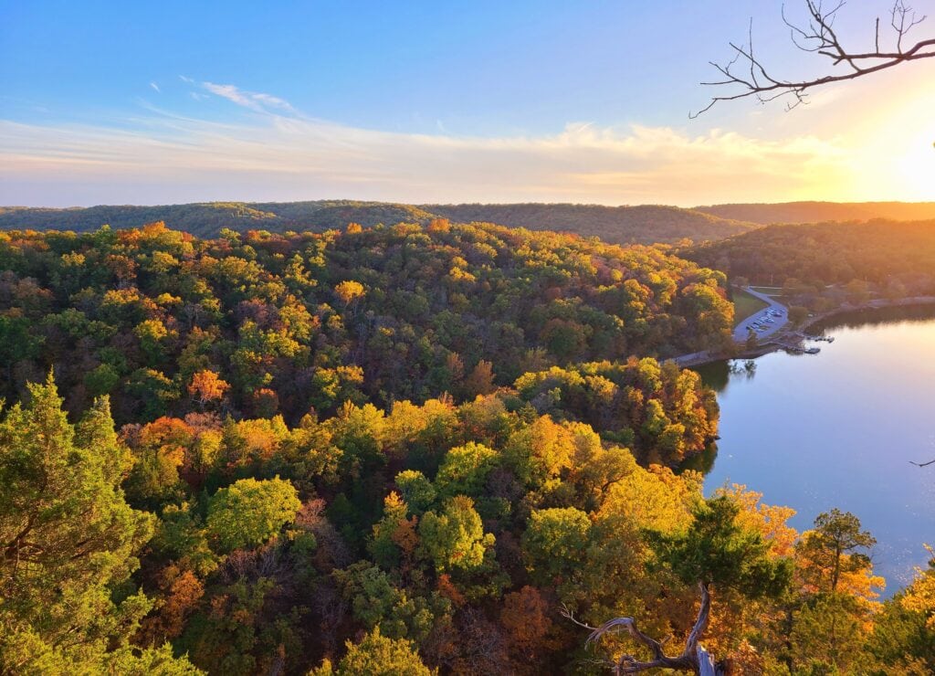 As the sun sets over Lake of the Ozarks, the golden light sweeps across a vibrant forest canopy, creating a breathtaking symphony of autumn colors