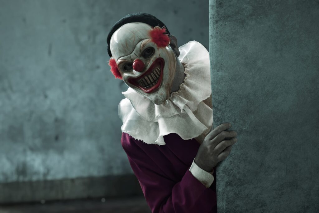 Man wearing scary clown mask peeking behind wall, Halloween theme