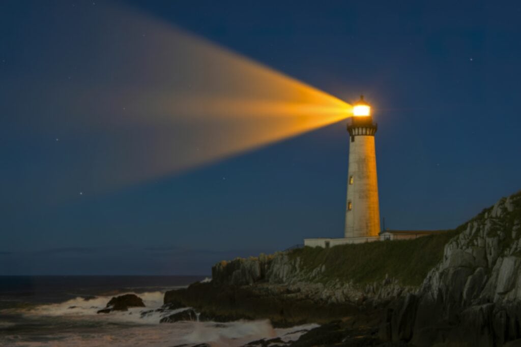 A photo of a lighthouse glowing brightly at night on the rocky coast