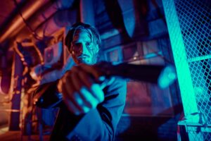 Portrait of a wounded action hero man aiming a gun in the light of the night city.