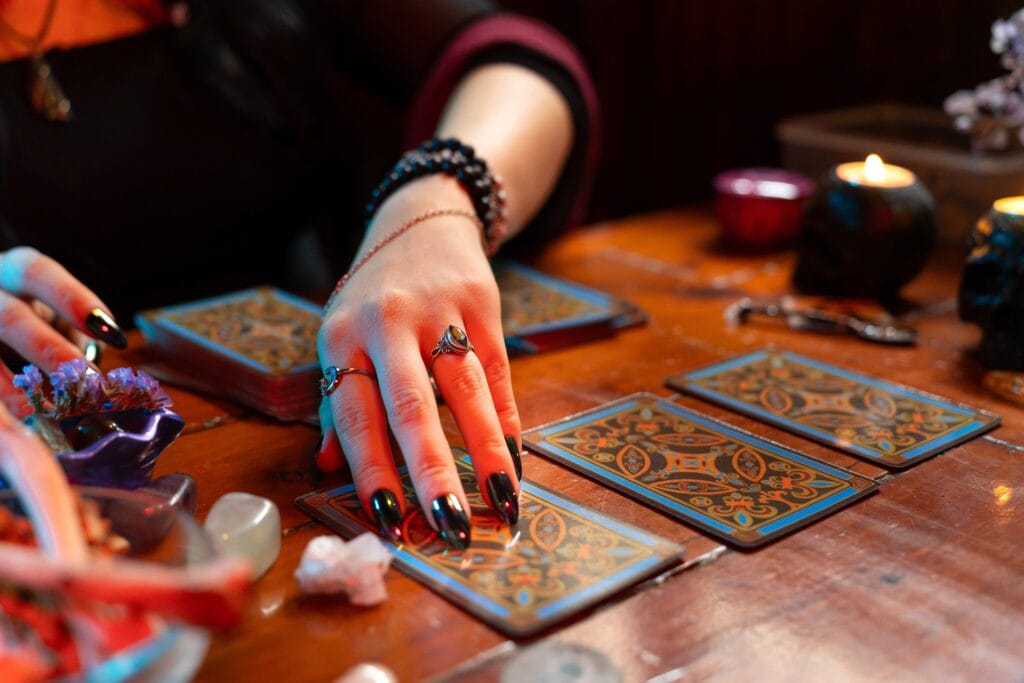 Fortune teller reading tarot cards on a wooden table with candles and crystals, predicting the future with esoteric and mystical arts