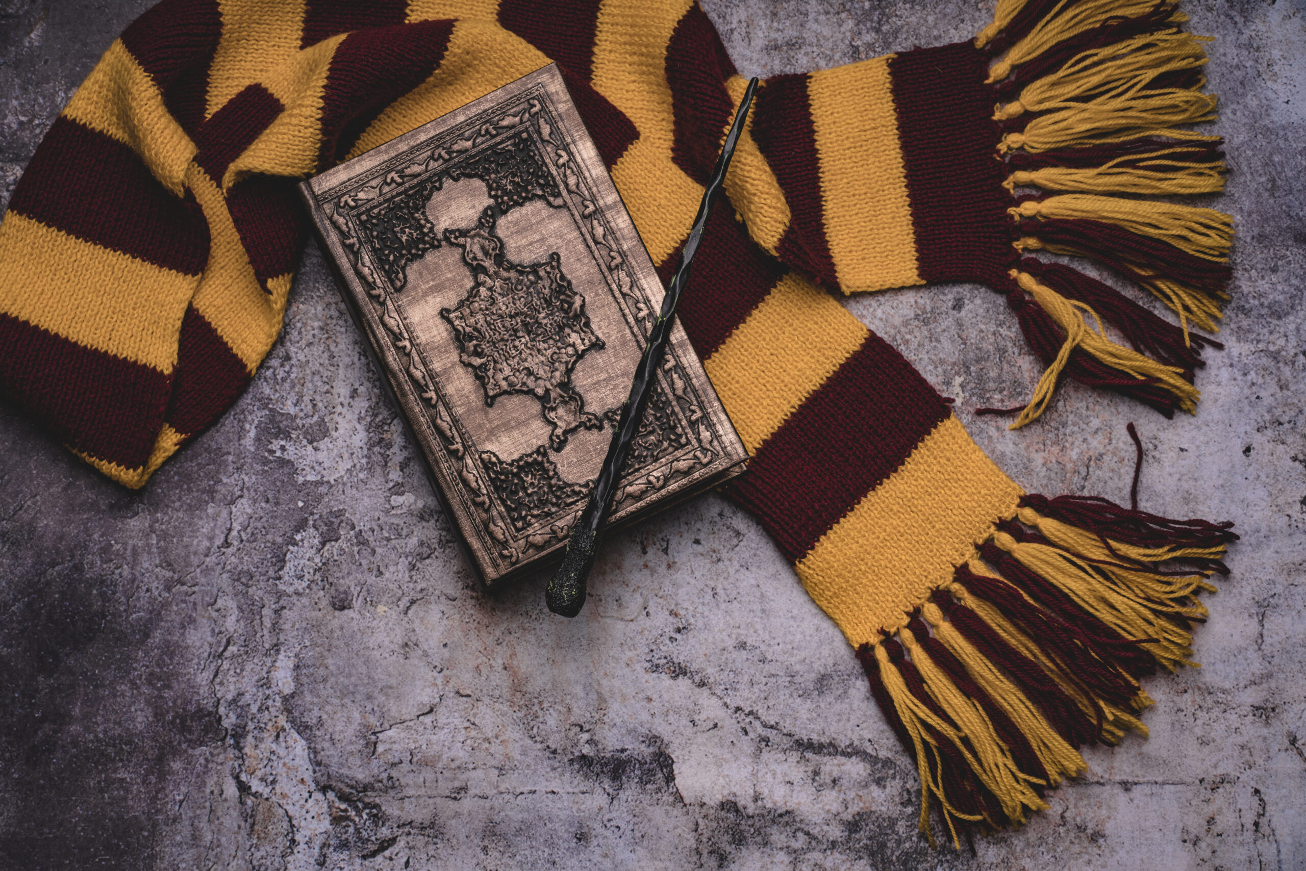 Subjects of the school of magic. Scarf, magic wand, book of spells on grey stone background.