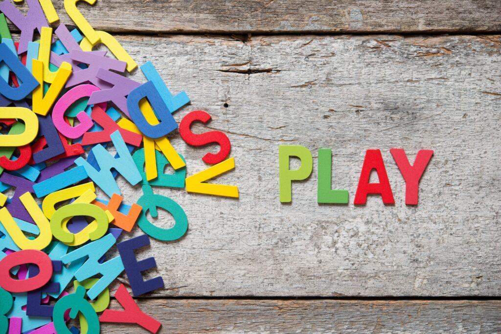 The colorful words -PLAY- made with wooden letters next to a pile of other letters over old wooden board.