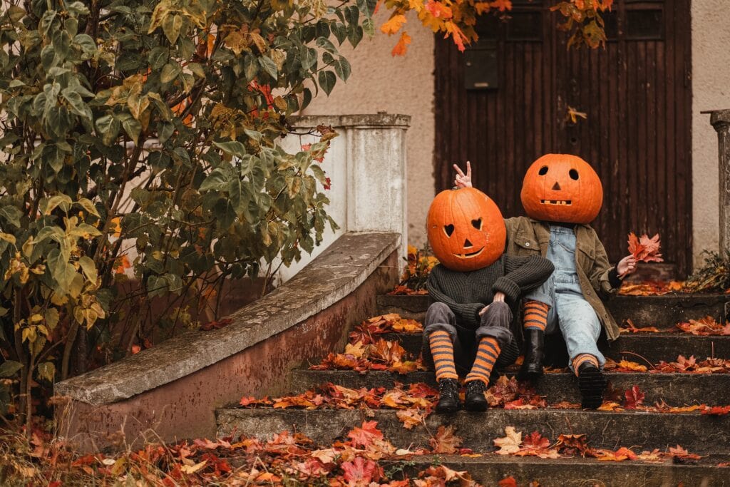 A charming duo with pumpkins on their heads, playing in a field of autumn leaves, celebrating the season.