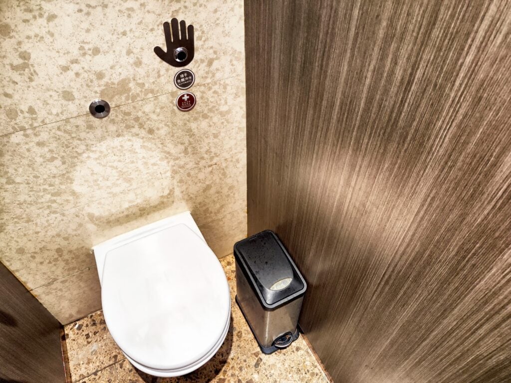 A clean and modern restroom features a white toilet with touchless controls and a waste bin, highlighting contemporary design elements.