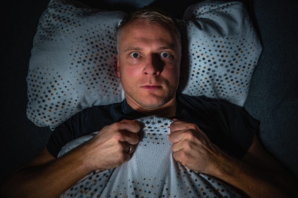 Man lies awake in bed at night with an anxious face