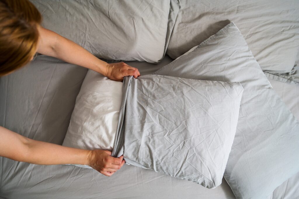 Female hands holding a pillow with fresh clean pillowcases, grey cotton bed sheets