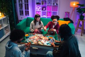 Diverse friends enjoying board game night, spending quality time together, playing cards, eating snacks, and having fun at home