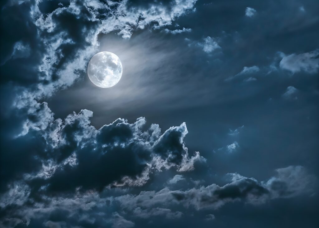 Full moon glowing in dark blue midnight sky with drifting clouds, creating spooky atmosphere for night and horror visuals