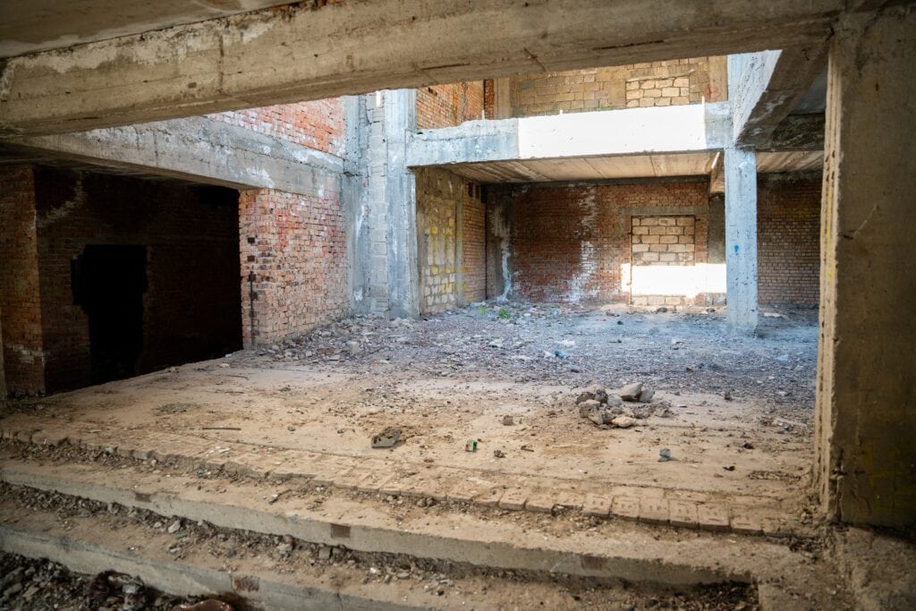 Abandoned building interior with exposed brick walls and concrete structures. Real estate development investment potential and architecture renovation opportunity.