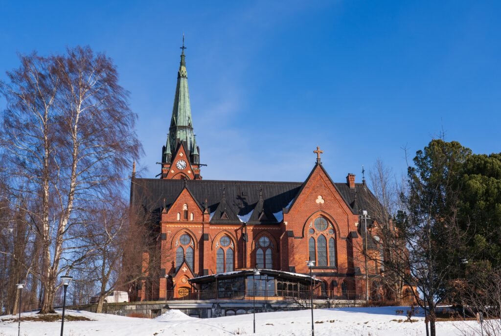 Majestic red brick neo-gothic church in Umeå, Sweden, featuring a tall green spire and arched windows, set in a snowy winter landscape
