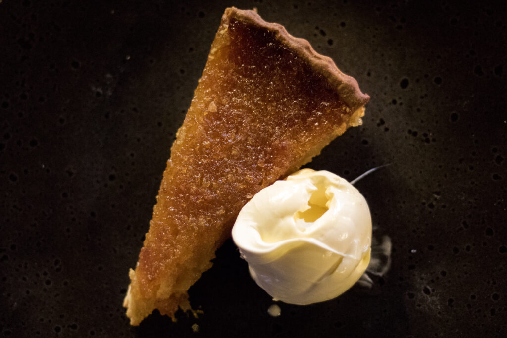 Treacle tart and cottage cream on a black plate